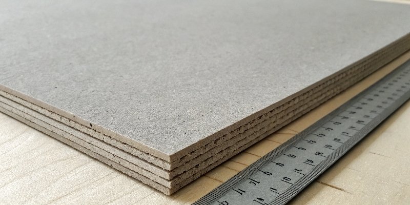A close-up of a thick greyboard sheet being measured