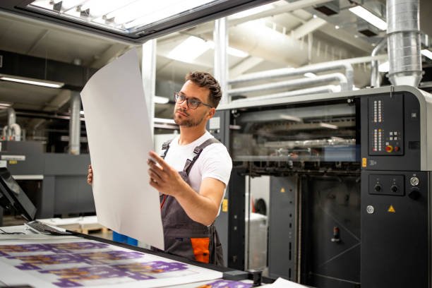 Print shop worker checking quality of imprint and controlling printing process.