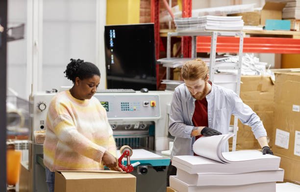 Portrait of two workers opening boxes with paper in industrial print shop, copy space